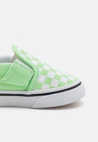 Zapatilla de lona de cuadros verdes y blancos, con suela de goma negra y panel lateral elástico para poner y quitar fácilmente.