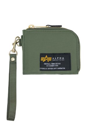 Olive green nylon wallet with gold zipper, featuring a black label with yellow logo, wrist strap, and compact rectangular design.