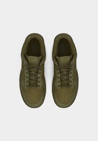 Ζευγάρι ελιάς πράσινα αθλητικά παπούτσια Nike με κορδόνια, φαίνεται από πάνω σε απλό ανοιχτό γκρι φόντο.