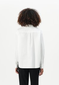 Camicia bianca con bottoni, maniche lunghe, dettaglio di pieghe sul retro e orlo dritto, realizzata in cotone liscio.
