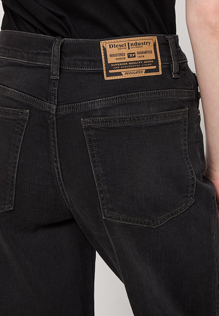 Jeans in denim nero con un'etichetta in pelle "Diesel Industry" sul retro. Presentano due tasche posteriori con cuciture visibili e un design slim fit.