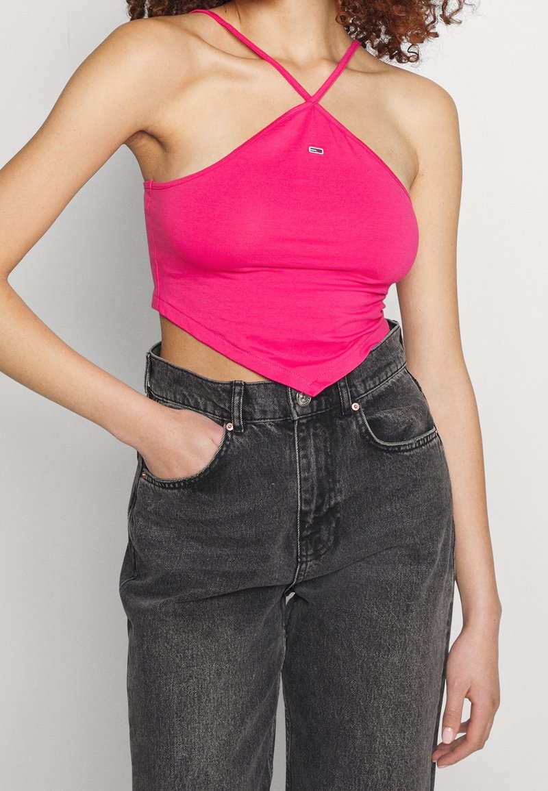 Top court rose ajusté avec des bretelles spaghetti, affichant un petit logo, associé à un jean en denim noir taille haute.