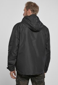 Zwarte geïsoleerde jas met een capuchon, voorzien van een gladde textuur en elastische manchetten. Het ontwerp is eenvoudig met een rechte snit.