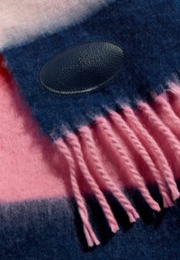 Vlnená deka s ružovými a námorníckymi pruhmi, s jemnou textúrou a strapcami na okrajoch. Obsahuje čiernu koženú nálepku s vyrazeným textom.