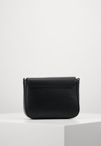 Borsa a tracolla nera in pelle con superficie testurizzata, chiusura a pattina e dettagli di cucitura sottili. Dotata di una tracolla regolabile.