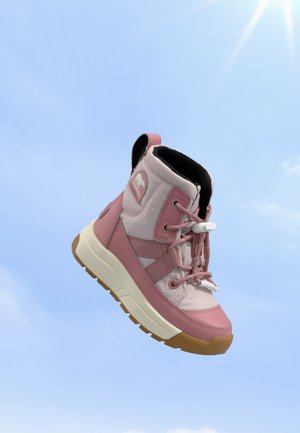 Basket montante rose et beige avec une semelle blanche épaisse et une semelle marron, flottant devant un ciel bleu clair avec la lumière du soleil.