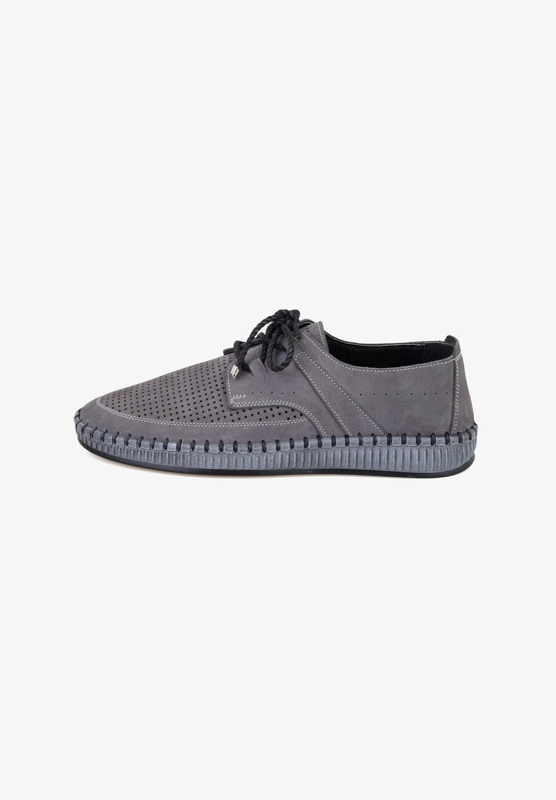 Chaussures en suede gris avec un design perforé, fermeture à lacets noire, et semelle en caoutchouc contrastante avec un détail de bord texturé.