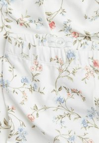 Witte stof met een bloemenpatroon met blauwe en roze bloesems, gedetailleerd met groene bladeren en een gestructureerde tailleband met een knop.