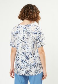 Blusa con motivo floreale in blu, bianco e crema, con maniche corte, scollatura rotonda e dettagli con pieghe sul retro.