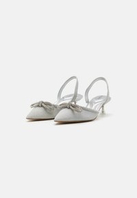 Srebrne slingback pete s ostrim nosom, teksturirano blago, ukrasna mašna i prozirni blok peto. Glatka unutrašnja površina.