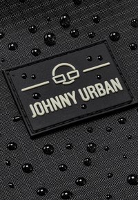 Black textured fabric with water droplets; features a raised black and cream label reading "JOHNNY URBAN."