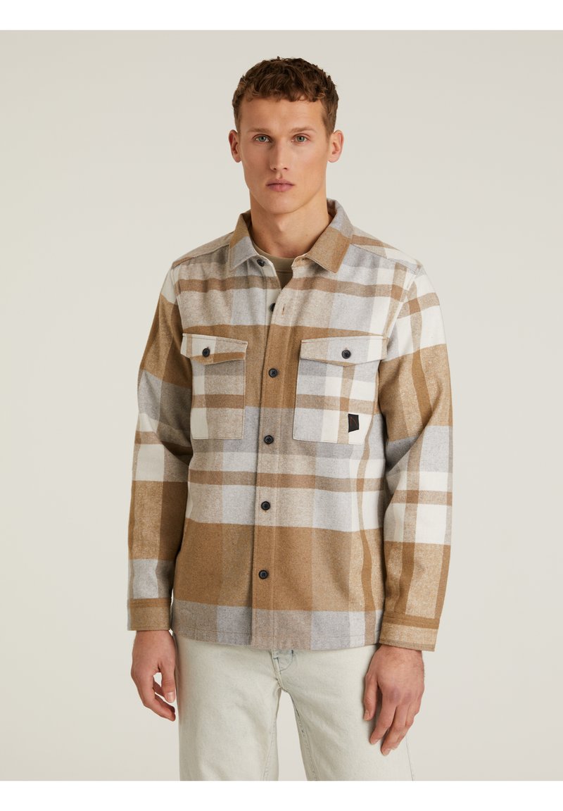 Camisa de cuadros marrón y gris con dos bolsillos en el pecho y botones negros. Hecha de un tejido texturizado, presenta bloques de color en contraste.