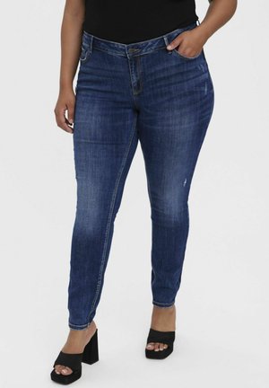 Skinny-Jeans aus dunkelblauem Denim mit distressed Akzenten und einem klassischen Fünf-Taschen-Design. Kombiniert mit schwarzen High-Heels.