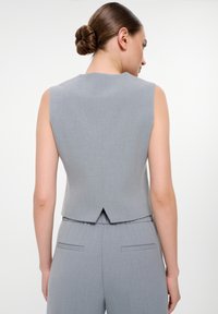 Bezramínkový šedý tailored top s kulatým výstřihem a rozparem na zadní straně, vyrobený z hladkého materiálu, kombinovaný s odpovídajícími kalhotami.