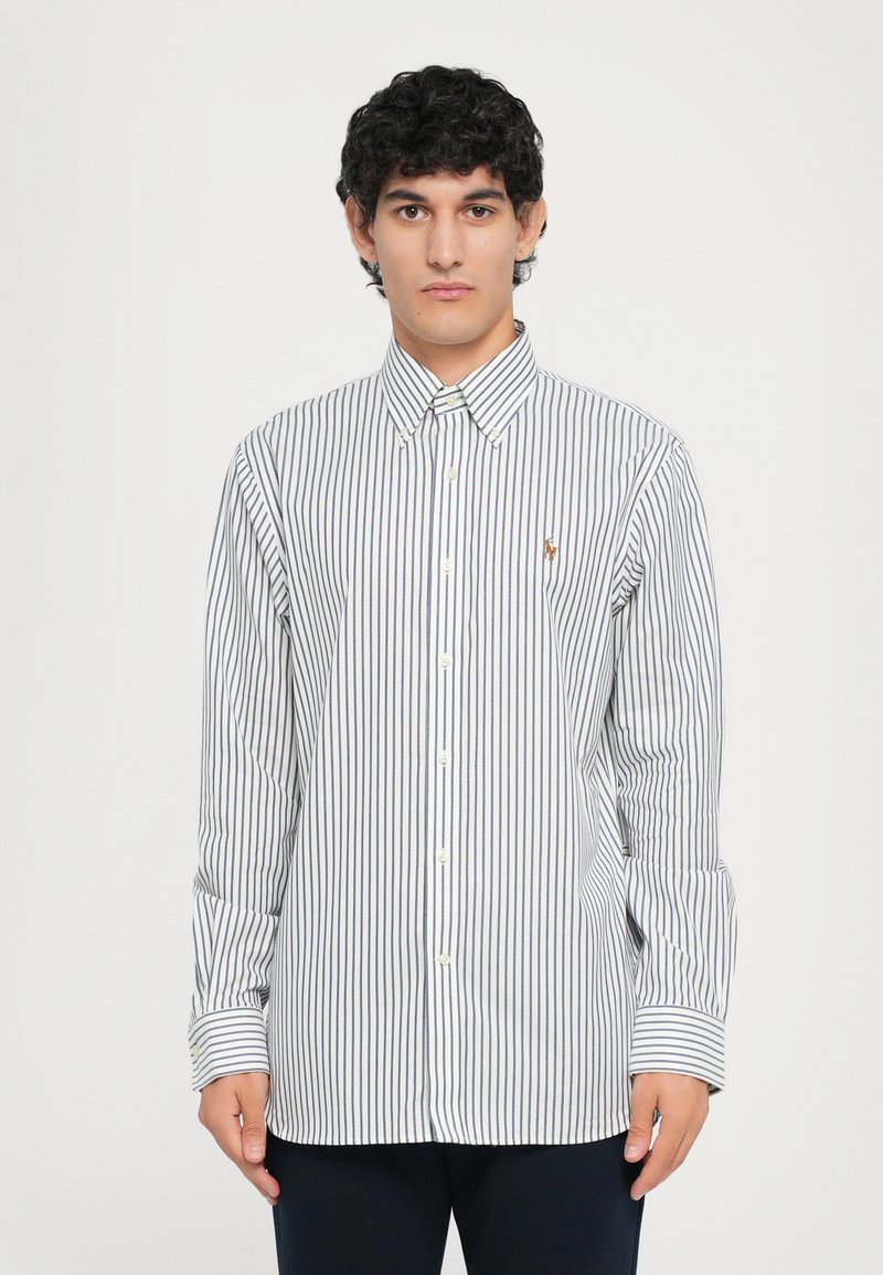 Chemise à boutons avec des rayures verticales bleu marine et blanches, à manches longues et col pointu. Petit logo brodé sur la poitrine.