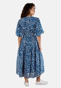 Blaues Blumen-Midi-Kleid mit Puffärmeln und gerafftem Bund, ausgestattet mit einem gestuften Rock und einem weißen Blumenmuster; kombiniert mit weißen Sneakers.