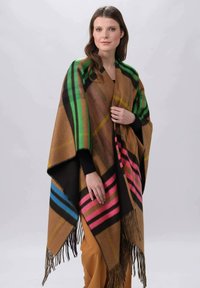 Poncho surdimensionné marron avec un motif à carreaux multicolore : rayures vertes, noires, roses et bleues. Dispose de franges le long des bords. Texture douce.