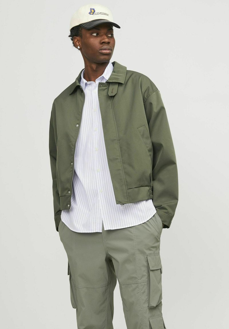 Veste verte légère avec un design à col, associée à une chemise blanche à rayures et un pantalon cargo olive. Comprend une casquette décontractée avec logo.