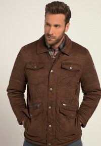 Brown suede jacket with quilted texture, snap closures, two chest pockets, and two side zippered pockets. Contrasting plaid shirt underneath.