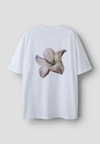 Hvid bomulds t-shirt med et stort, fotografisk tryk af en lys pink blomst med lilla accenter på ryggen. Korte ærmer, afslappet pasform.