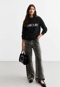 Zwarte trui met witte "AMOUR" opdruk, gecombineerd met grijze panterprintbroek. Geaccentueerd met een kleine zwarte handtas en zwarte schoenen.