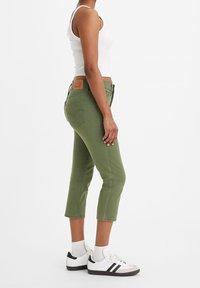 Oliwkowe, krótkie jeansy z dopasowanym krojem, pięcioma kieszeniami i markową skórzaną naszywką na pasku. Noszone z białym podkoszulkiem i trampkami.