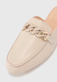 Beige Leder Slipper mit flachem Design, ausgestattet mit einem klobigen Kettenakzent und gesteppten Details entlang der Kanten.