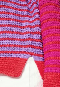 Maglione lavorato a maglia con strisce orizzontali in rosso, viola e rosa. Tessuto testurizzato con orlo curvo e polsini a coste.
