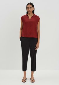 Top rosso a maniche corte con colletto abbinato a pantaloni neri lunghezza caviglia e infradito nere. Tessuto morbido con una vestibilità comoda.