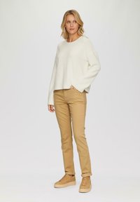 Maglione bianco a trama, pantaloni beige aderenti e sneakers color crema. Il maglione ha maniche lunghe e scollo rotondo. I pantaloni hanno una vestibilità slim.