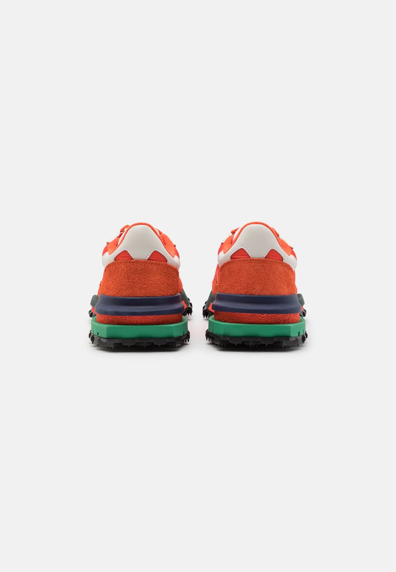 Zapatillas de ante rojas con acentos blancos, que cuentan con una suela multicolor en verde, azul y negro. Diseñadas para uso al aire libre, con una banda de rodadura prominente.