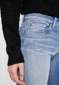 Jasnoniebieskie dżinsy z wybielanym wykończeniem, z klasycznym pięcio-kieszeniowym krojem oraz czarnym, teksturowanym swetrem przy rękawie.