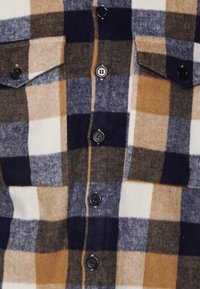 Brun, blå och beige rutmönstrad flanellskjorta med två bröstfickor, svarta knappar och en mjuk textur.