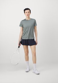 Sporta apģērbs, kas sastāv no gaiši pelēka īsām piedurknēm krekla un tumši zila tenisa svārku, apvienots ar baltām sporta kedām un tenisa raketi.