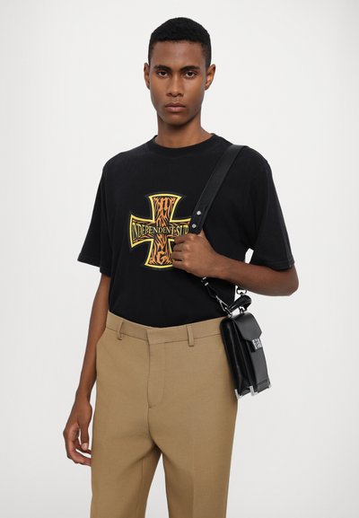 T-shirt nera in cotone con grafica a motivo tigre, abbinata a pantaloni beige sartoriali. Borsa a tracolla nera con accenti argentati.