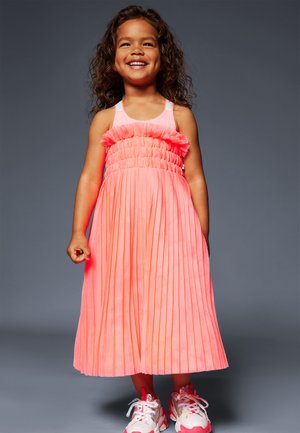 Robe plissée néon rose avec corsage froncé et bretelles. Portée avec des baskets blanches et roses, dotées d'une semelle épaisse et d'accents colorés.