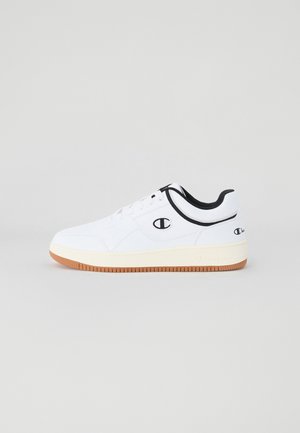 Baskets blanches avec une tige lisse, accents noirs sur le col et le logo, et une semelle en caoutchouc gomme. Design à lacets, bout rond.