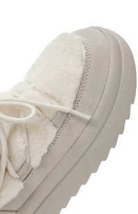 Zapatillas de ante en color beige claro con detalles de piel de oveja suave, parte superior de ante y cordones planos. Presenta una suela gruesa y texturizada con un patrón de olas.