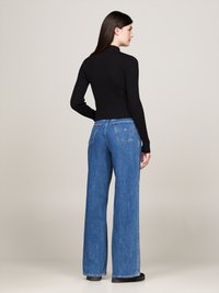 Top nero a righe con maniche lunghe abbinato a jeans blu a gamba larga con vita alta, dotato di due tasche posteriori e orlo pulito.