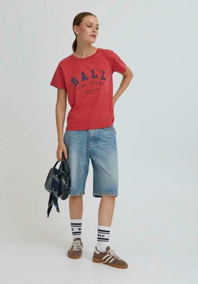 T-shirt en coton rouge avec un graphique "BALL", shorts en denim bleu, sac à main noir, chaussettes rayées blanches et noires, et baskets brunes.