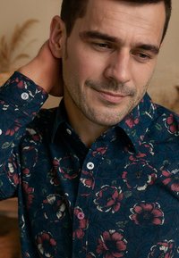 Bloemenpatroon shirt in donkerblauw, met grote rode en witte bloemen, knoopsluiting kraag en contrasterende knopen in wit en roze.