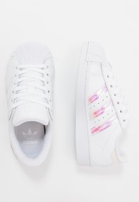 Sneakers bianchi con parte superiore in pelle testurizzata, dettagli perforati e strisce rosa metalliche sui lati. Suola in gomma classica.