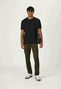 Μαύρη κοντομάνικη μπλούζα, ελαιόχροια παντελόνι, μαύρη τσάντα σωματική. Τα αξεσουάρ περιλαμβάνουν γυαλιά ηλίου και λευκά αθλητικά παπούτσια με μαύρες ρίγες.