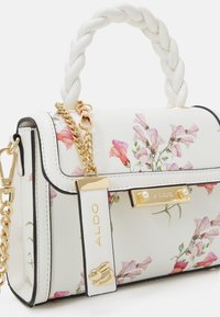 Biała torebka z kwiatowym wzorem, złotym wykończeniem, plecionym uchwytem u góry i łańcuszkowym paskiem. Oferuje metkę z logo oraz perłowe akcenty na zapięciu.