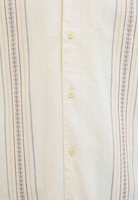 Camisa de botones de color claro con rayas bordadas verticales en rojo, naranja, verde y azul, y con un tejido texturizado. Se pueden ver seis botones.