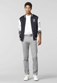 Zwart-witte bomberjack met gestreepte boorden, grijze broek en witte sneakers. Het jack heeft een logo-detail op de borst.