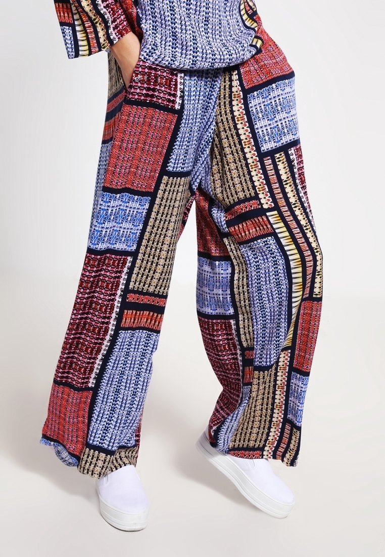 Pantalon ample à jambes larges avec un motif patchwork géométrique multicolore, porté avec des chaussures blanches sans lacets et un haut assorti.