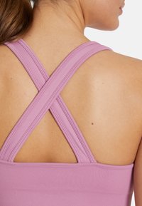 Purple athletic top with crisscross straps, ribbed texture, and a fitted design. Shows back view and shoulder area. Smooth fabric finish.