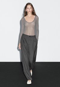 Grijze langekorte sheer top met een ronde hals, gecombineerd met hoge taille donker gestreepte broeken en lichtgekleurde platte schoenen.