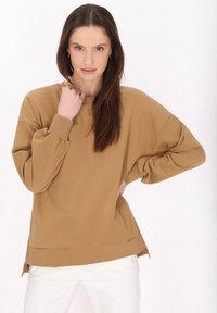 Felpa marrone oversize con maniche lunghe, polsini a costine e scollatura rotonda. Fessure laterali importanti all'orlo per una vestibilità rilassata.